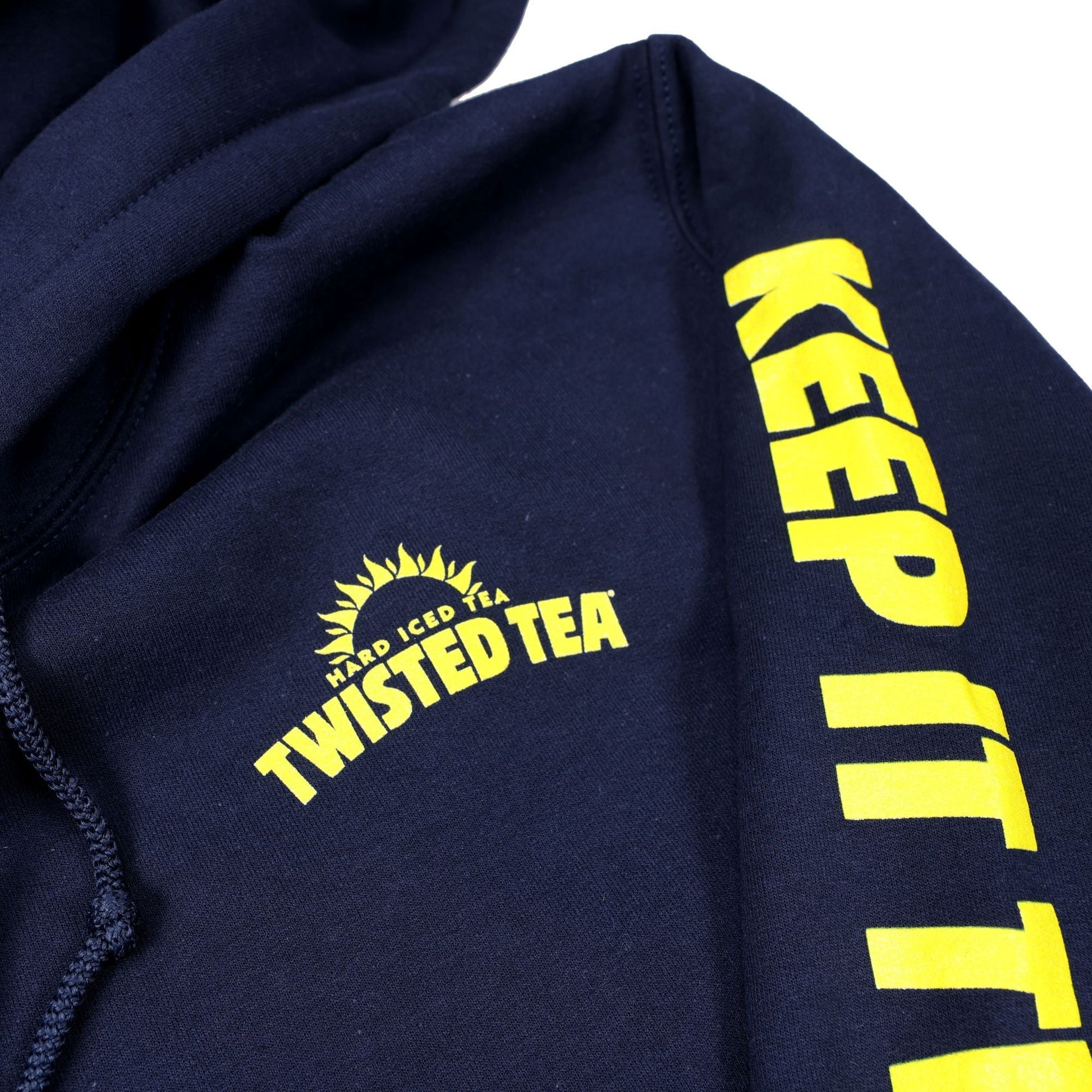 Close up of logos Navy blue pullover hoodie with small yellow sun Twisted Tea logo and keep it twisted down the left sleeve
