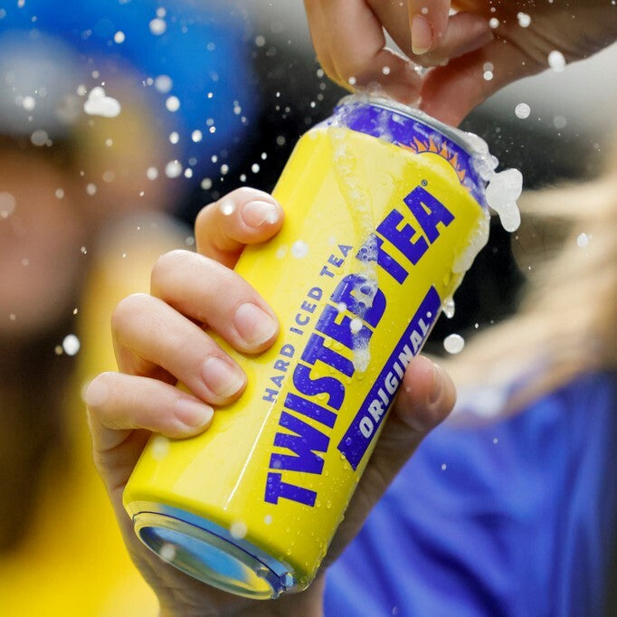 Close‑up action shot of a hand opening a yellow Twisted Tea Original hard iced tea can, with liquid splashing around the top of the can and bold blue Twisted Tea branding clearly visible.
