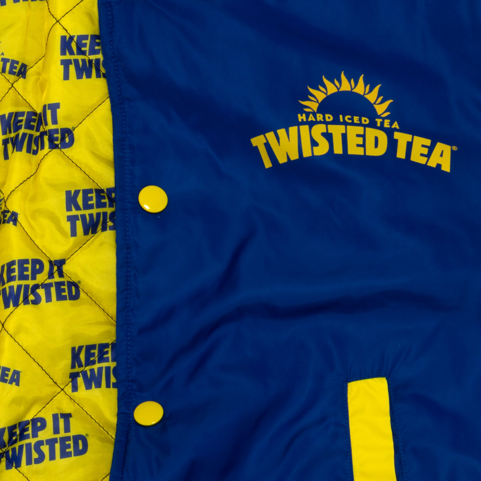 Close-up of a blue and yellow jacket or vest with the Twisted Tea logo printed in yellow on the chest and a yellow quilted lining with repeated 'KEEP IT TWISTED' text along the side.