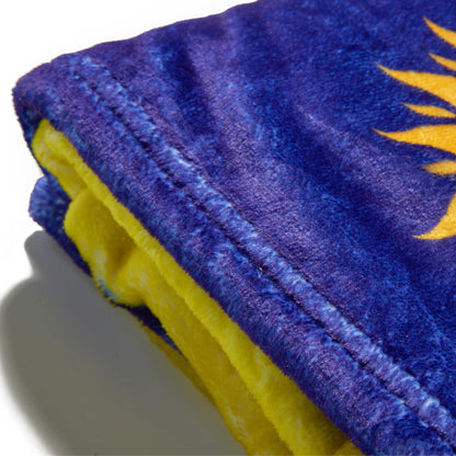 A close-up of a plush fleece blanket showing its purple exterior with a yellow sun graphic and a bright yellow fleece lining.